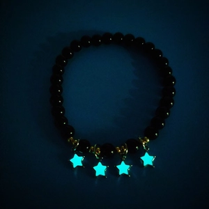 Leuchteffekt der sternförmigen Anhänger an schwarzem Perlenarmband in der Dunkelheit