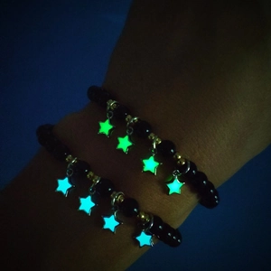 Leuchtende Sternanhänger an schwarzen Perlenarmbändern, die grün und blau leuchten