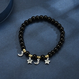 Detail von Onyx-Perlenarmband mit goldenen Sternen und Mondanhängern auf blauem Stoff