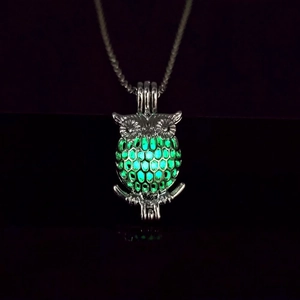 Detailed macro view of silver owl pendant glowing green in dark environment