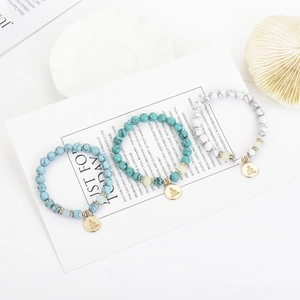 Detailansicht von Leuchtperlen und goldenen Buddha-Anhängern auf den Yoga-Armbändern