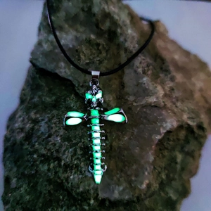 Gothic skull cross necklace with green luminous glow on rugged stone display