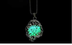 Close-up of glowing Valknut pendant with green luminous effect on black background