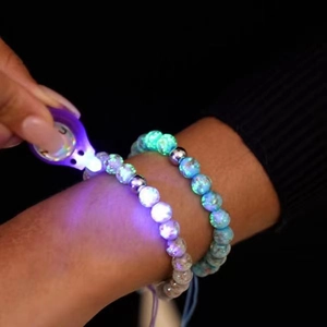 Luminous crystal glass beads bracelet showing bright blue glow under purple LED light macro
