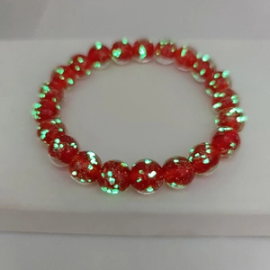 Close-up of red luminous crystal glass beads with green glowing spots on elastic bracelet