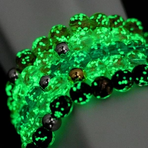 Macro shot of luminous green glow-in-the-dark beads and metallic accents on a healing bracelet