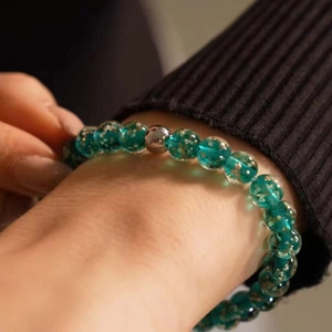 Detailed view of luminous green star glass beads bracelet on a wrist over black knitwear