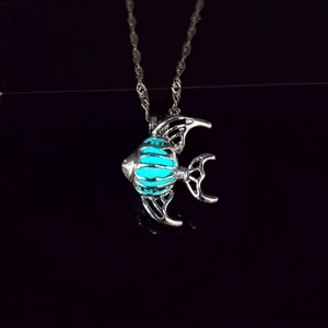 Détail macro d'un collier pendentif poisson lumineux avec un cœur bleu sur fond noir
