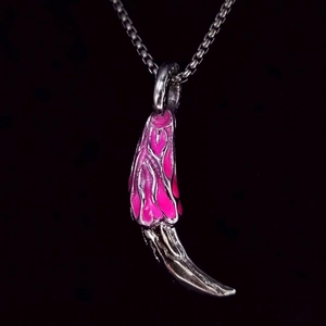 Detail of a punk-style wolf tooth pendant featuring pink heart enamel and silver metal chain