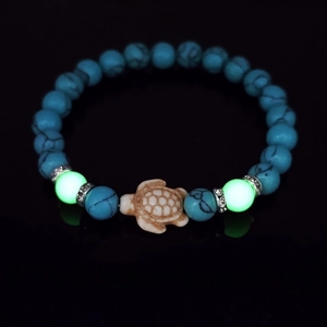 Macro view of blue turquoise bead bracelet with glowing turtle charm and silver spacers