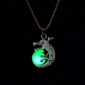 Détail d'un pendentif dragon argenté tenant une pierre lumineuse verte sur fond noir