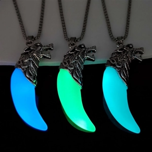 Luminous wolf tooth pendant showing glowing blue, green, and cyan colors in the dark