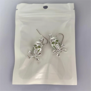 Close-up of silver skull and crossbones hook earrings with luminous green details