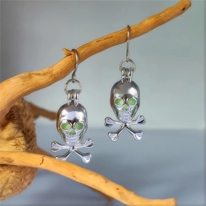 Gothic skull crossbones drop earrings with green glowing eyes on a rustic wood branch