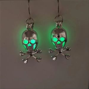 Detailed view of silver skull earrings with green luminous glow in the dark features