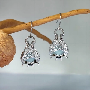 Close-up of silver hollow bat earrings with blue glowing beads on a dark wood branch