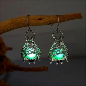 Gothic hollow bat earrings with green luminous glow hanging on a wooden branch