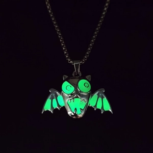 Macro view of Halloween demon wings necklace showing glowing green luminous effect in the dark