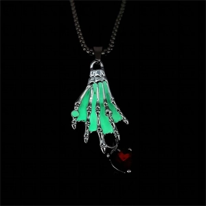 Primer plano de colgante gótico de mano de esqueleto con brillo verde y circón de corazón