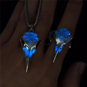 Macro view of glowing blue Vegvisir viking bird skull ring and necklace set in darkness