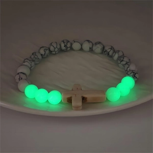 Perle luminose che brillano al buio su un bracciale con croce in pietra marmorea