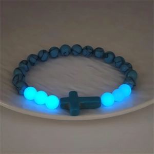 Dettaglio macro del bracciale luminoso con ciondolo a croce e perline blu al buio