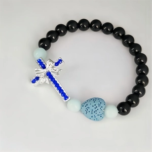 Détail du bracelet perlé avec pierre de lave, perle de cœur et pendentif croix bleue