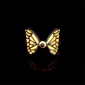 Macro shot of luminous butterfly ring with orange gradient wings and black bead on dark band