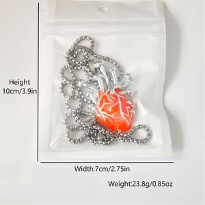 Dettaglio della collana argentata con cuore anatomico rosso e piccoli funghi
