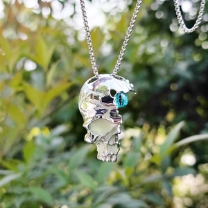 Detailed view of silver skull necklace with luminous blue cat eye stone set in the eye socket