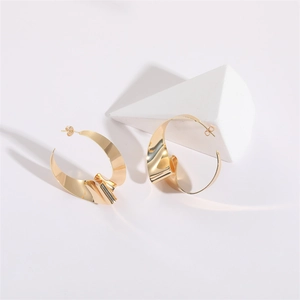 Detail of chunky gold knot earrings with irregular pleated texture on white pedestal