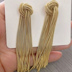 Detail showing gold snake chain tassel earrings with woven knot design on white card