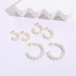Three sizes of C-shaped pearl hoop earrings with gold studs on a clean minimalist background