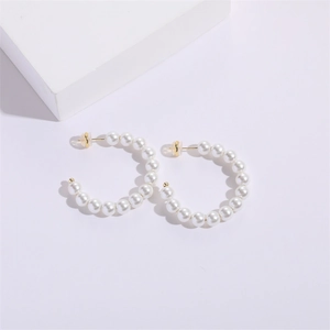 Detail view of C-shaped earrings with white pearls and gold metal base on stone pedestal