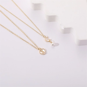 Detail of gold heart pendant with letter B and moon necklace with pearl on white wave stand