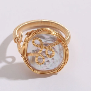 Primer plano de un anillo artesanal de hilo dorado con perla de agua dulce natural