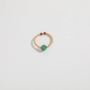Detailed view of an adjustable gold ring with a green bead and red-brown accents
