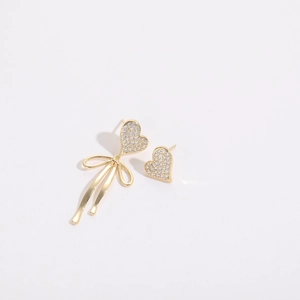 Detail of asymmetric 14K gold plated heart and bow earrings with micro-inlaid rhinestones