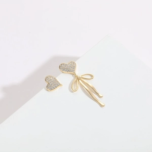 Macro detail of asymmetric heart earrings with ribbon bow and micro-pave white zircons