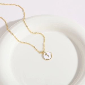 Detail of a 14K gold plated necklace featuring a white enamel rose flower coin pendant