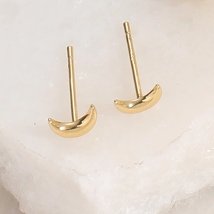 Detail showing polished gold-plated crescent moon stud earrings on a natural stone surface