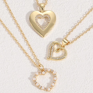 Macro detail of three gold heart necklaces featuring zircon stones and white faux pearls