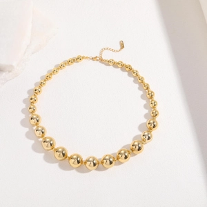 Macro detail of 18K gold-plated beaded necklace showing lobster clasp and 18K tag