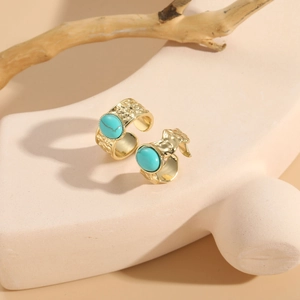 Close-up of gold hammered adjustable rings with oval turquoise stone on beige pedestal