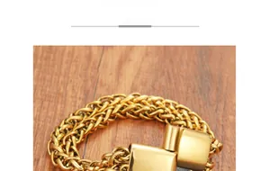 Dettaglio di bracciale a catena a spiga dorata con grande chiusura quadrata su legno