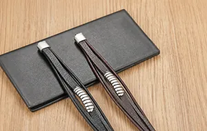 Detailaufnahme von geflochtenen Lederarmbändern mit Metallelementen auf dunklem Portemonnaie