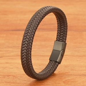 Detail of dark brown braided leather bracelet featuring a matte black magnetic clasp and wood texture