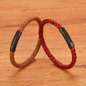 Detail van gevlochten leren armbanden met matzwarte magnetische sluitingen op hout