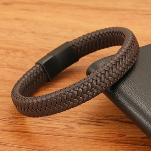 Detail of multi-strand braided brown leather bracelet with matte black metal clasp on wood