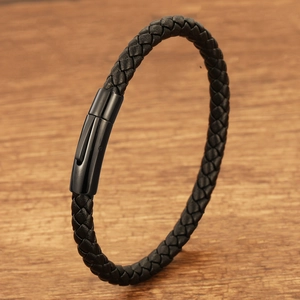 Detail of black braided leather men's bracelet with a glossy black metal clasp on wood
